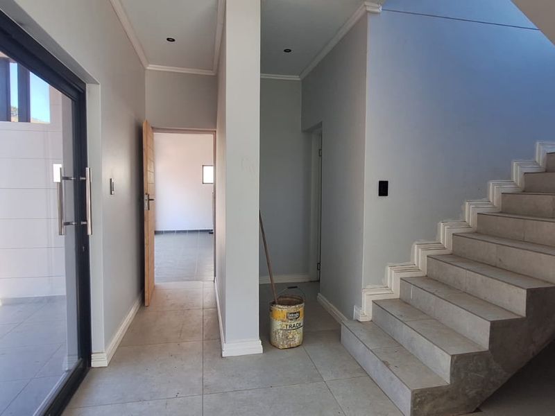 A bright, modern entrance hallway featuring tiled flooring, a contemporary staircase, and a large sliding glass door providing access to the exterior.