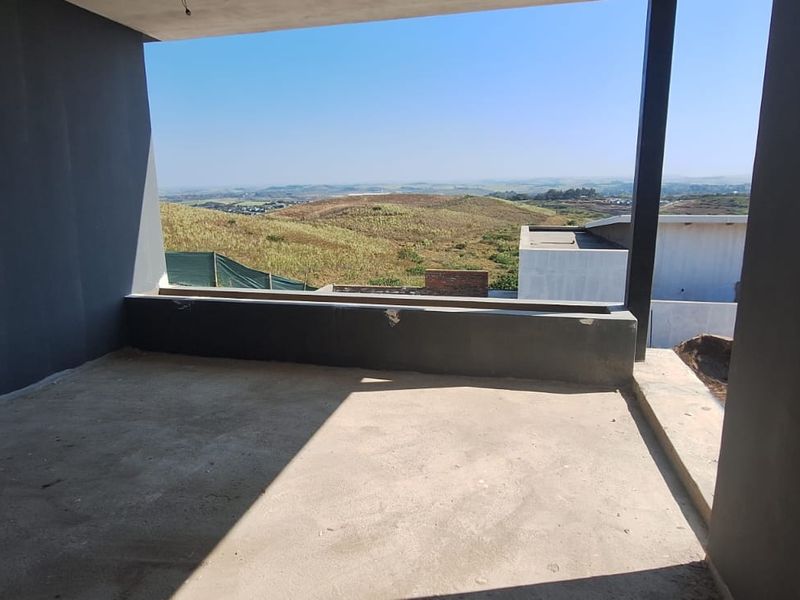 An unfinished balcony or patio area featuring raw concrete flooring and plastered walls, offering expansive views of the surrounding landscape.