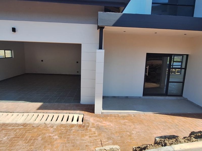 Modern front facade featuring a double garage with tiled flooring, a glass panel entrance door, and a paved driveway area.