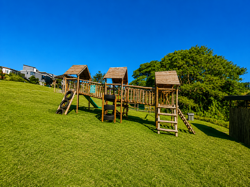 A well-maintained outdoor garden area featuring a large wooden playground structure set on a spacious, manicured lawn.