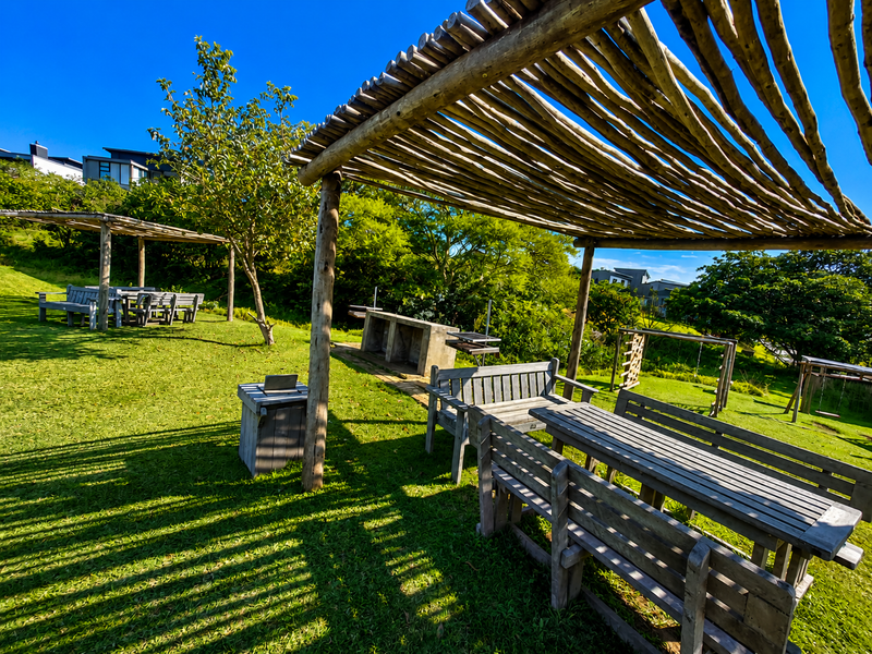 A spacious outdoor garden area featuring a rustic wooden pergola, built-in concrete braai, and well-maintained lawn, ideal for outdoor entertaining.