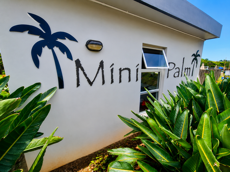 Exterior view of the property facade featuring modern signage, a top-hung window, and an external wall light, surrounded by lush garden foliage.