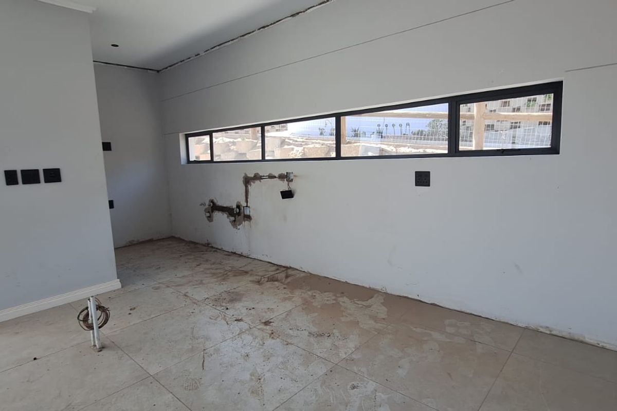 An unfinished kitchen space featuring tiled flooring, horizontal windows, and exposed plumbing rough-ins, ready for cabinetry and final finishes.