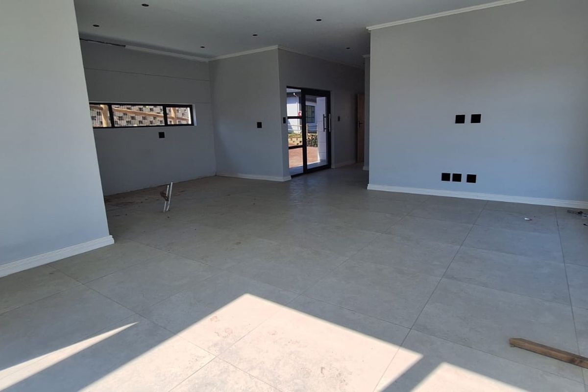 Spacious, open-plan living area featuring large format floor tiles, modern aluminium window frames, and recessed downlighting, currently in a near-complete state.