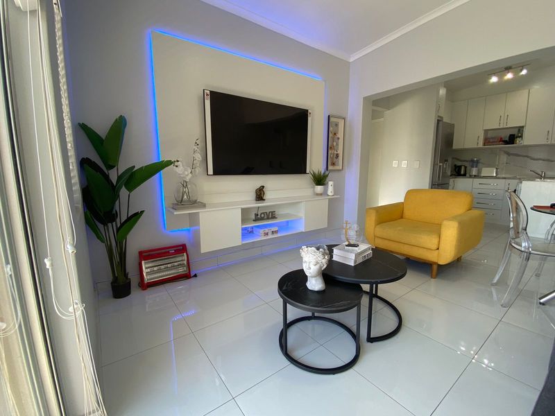 Modern open-plan living area featuring polished floor tiles, a custom built-in media unit with integrated LED lighting, and an adjacent contemporary kitchen.