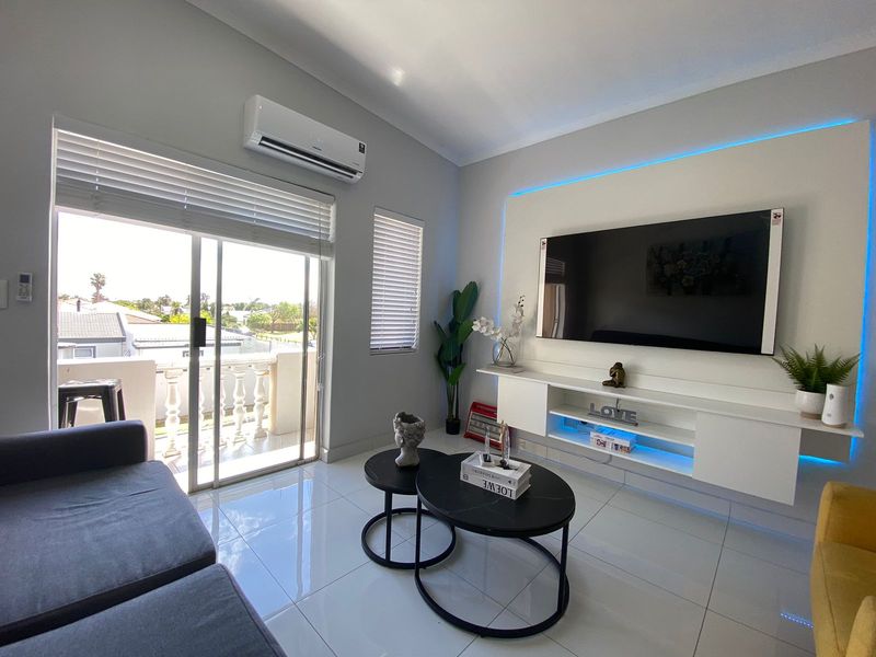 Modern living room featuring tiled floors, a built-in media console with LED accent lighting, split-system air conditioning, and sliding glass doors leading to a balcony.