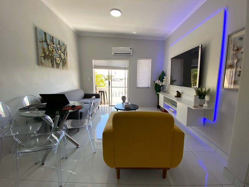 Modern living room featuring tiled flooring, a floating media console with integrated LED lighting, split-system air conditioning, and access to a private balcony.