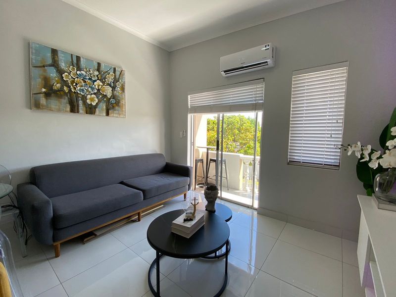 A bright living room featuring polished porcelain floor tiles, a wall-mounted split-system air conditioner, and sliding glass doors leading to a private balcony.