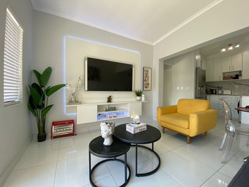 Modern open-plan living area featuring a built-in media console with LED lighting, tiled floors, and a seamless transition to a contemporary kitchen.