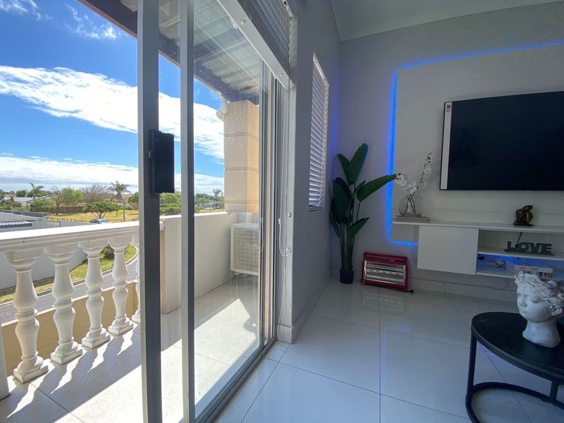 Modern living room featuring sleek tiled floors, a built-in media unit with ambient lighting, and direct access to a private balcony with balustrade.