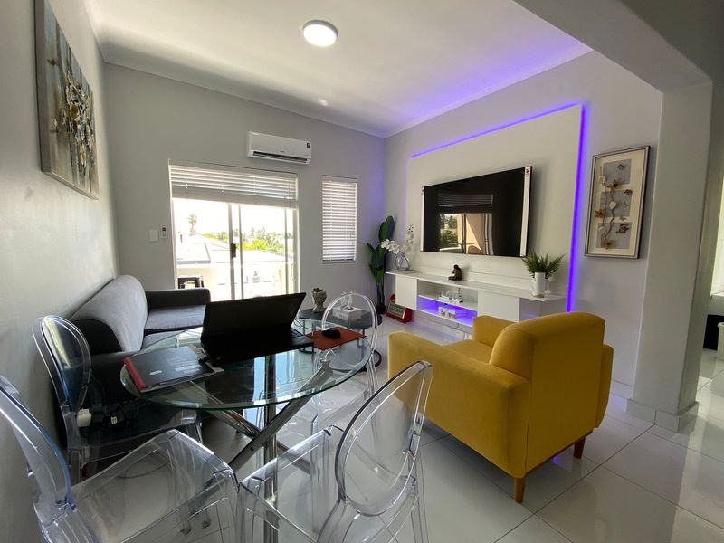 Modern living room featuring tiled flooring, a built-in media console with integrated LED lighting, and a split-system air conditioner with access to a balcony.