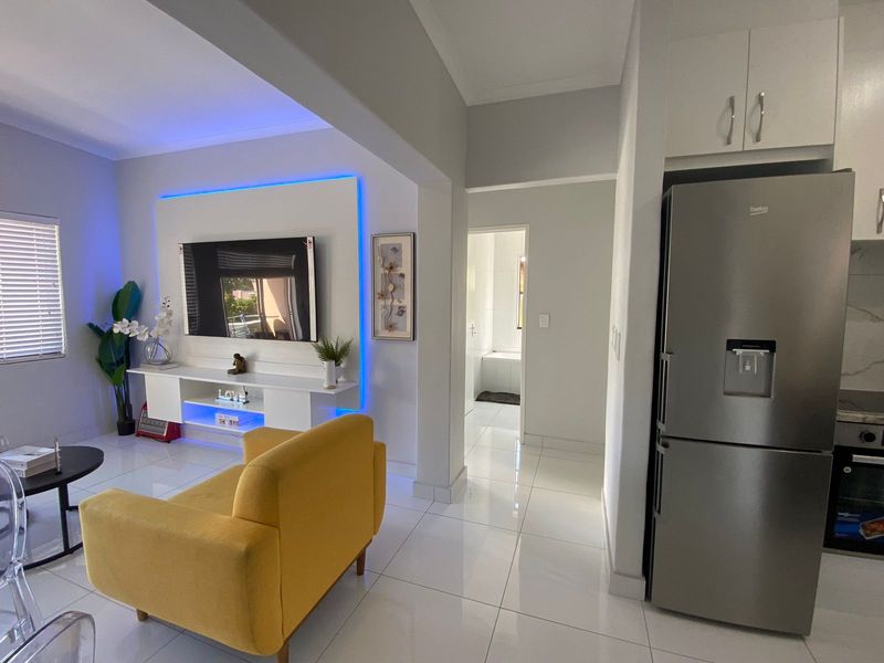 Modern open-plan living area featuring sleek porcelain tiles, built-in media unit with ambient LED lighting, and a seamless transition to the kitchen and hallway.