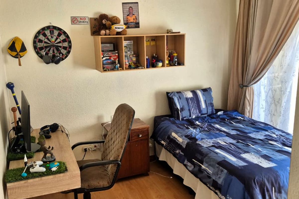 A compact bedroom featuring laminate flooring and natural light through a window with curtain tracks, suitable for a single bed and study area.