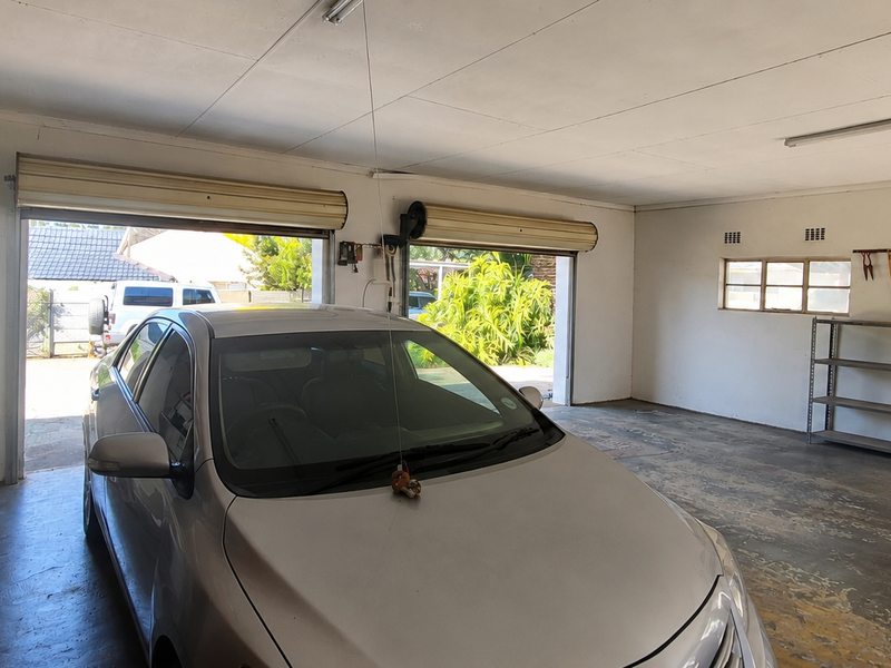 Spacious double garage featuring roller shutter doors, concrete flooring, and fluorescent lighting, providing ample room for vehicle storage and workshop space.