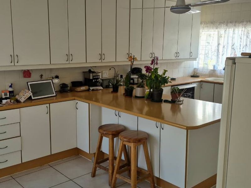 A functional kitchen featuring white cabinetry, laminate countertops, and tiled flooring, offering a practical layout with potential for modern updates.