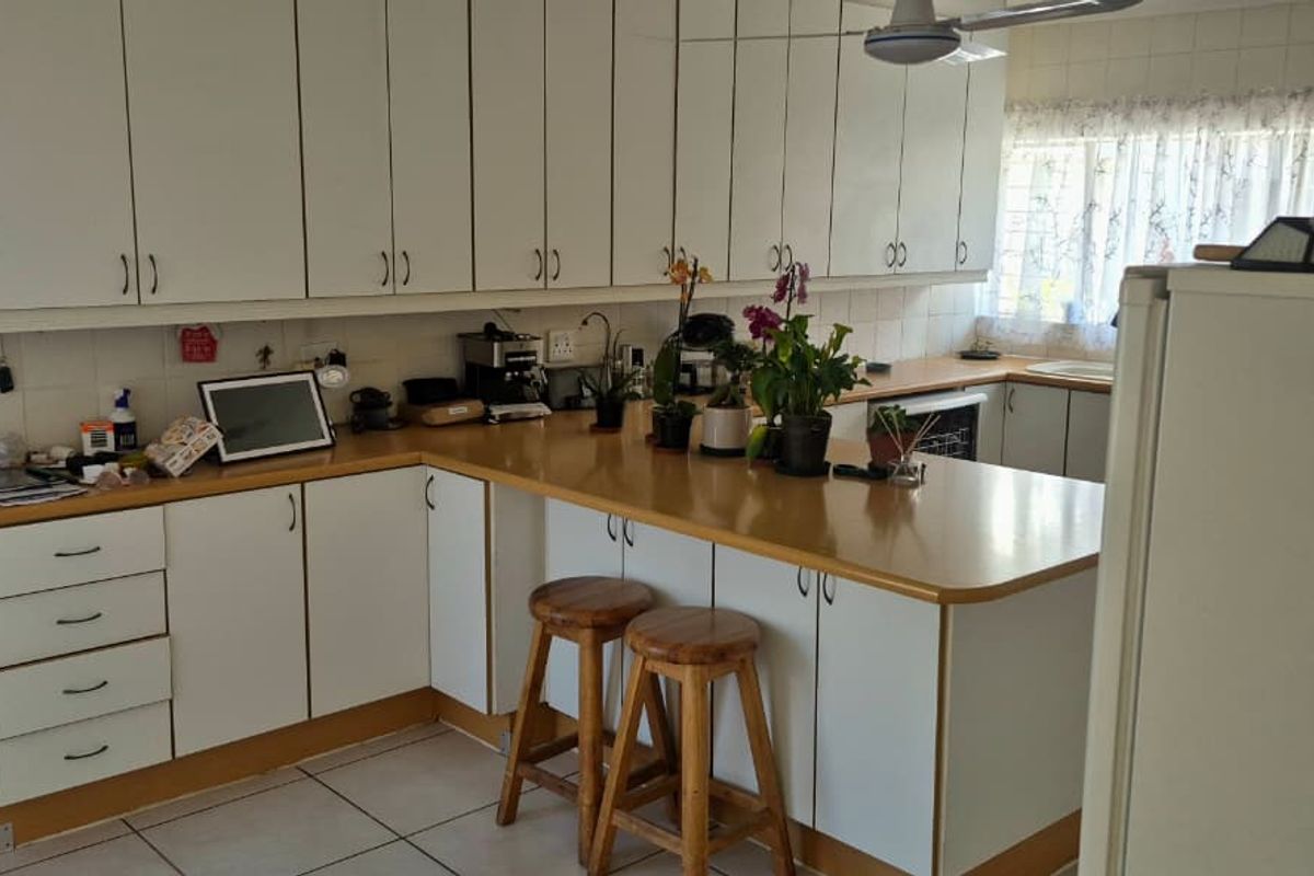 A functional kitchen featuring white cabinetry, laminate countertops, and tiled flooring, offering a practical layout with potential for modern updates.