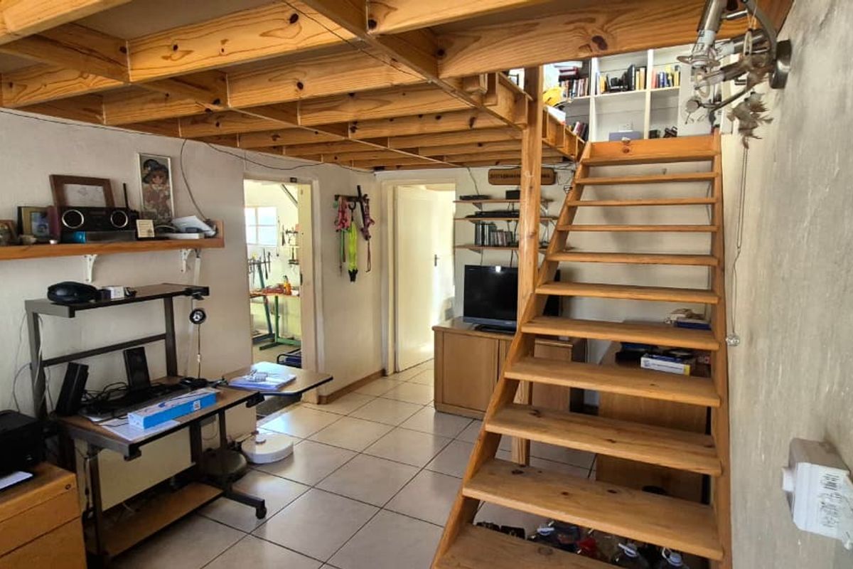 Living area featuring exposed timber ceiling beams, a wooden staircase leading to a mezzanine level, and tiled flooring throughout.