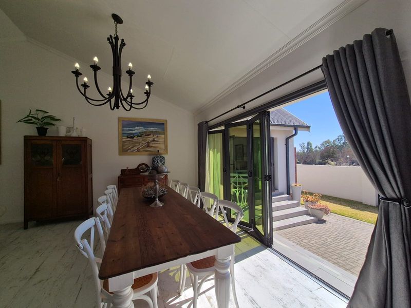 Bright dining room featuring vaulted ceilings, elegant crown molding, and large folding glass doors that open onto a paved patio area.