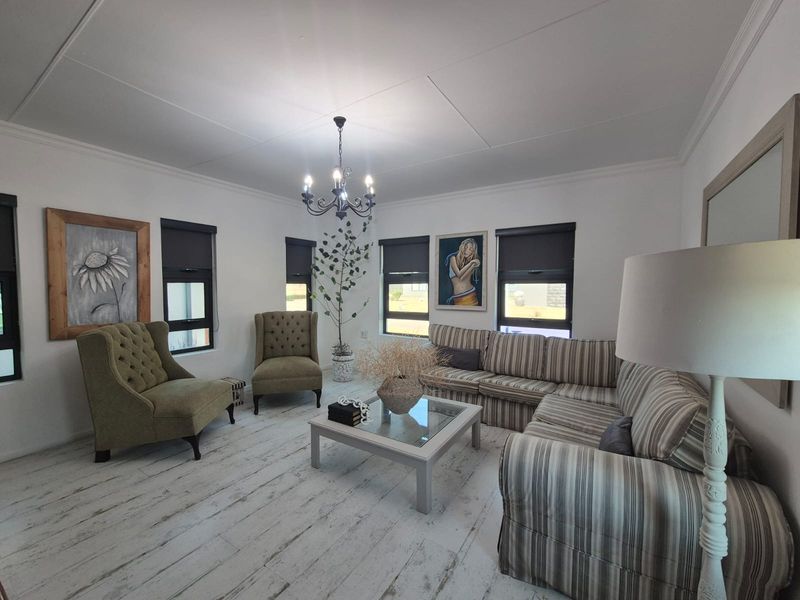 A bright and well-maintained living room featuring timber-look flooring, modern roller blinds, and a decorative chandelier.