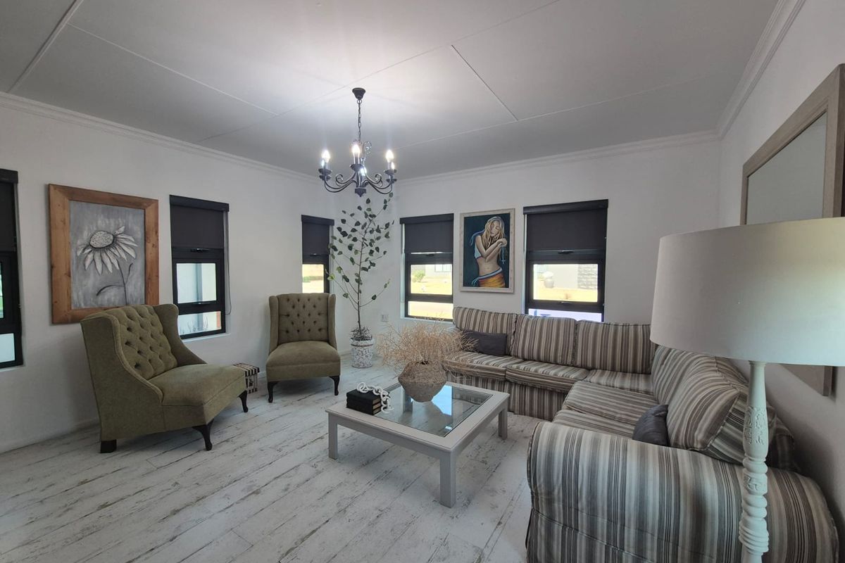 A bright and well-maintained living room featuring timber-look flooring, modern roller blinds, and a decorative chandelier.