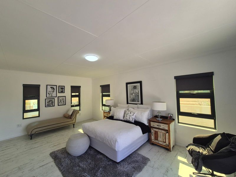 Spacious bedroom featuring modern black aluminium window frames, roller blinds, and light-toned laminate flooring with a clean, neutral aesthetic.