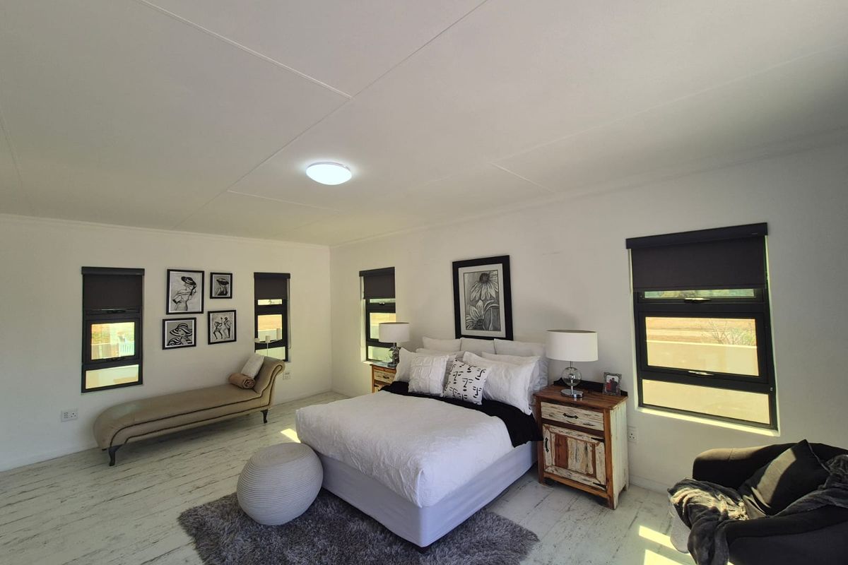 Spacious bedroom featuring modern black aluminium window frames, roller blinds, and light-toned laminate flooring with a clean, neutral aesthetic.