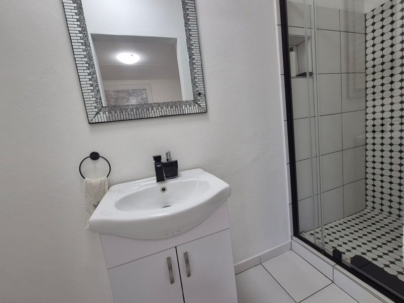 A modern bathroom featuring a white vanity cabinet with a ceramic basin and a glass-enclosed shower with decorative patterned tiling.