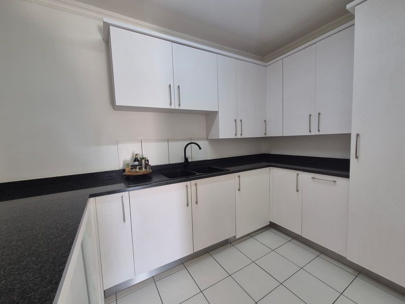 A clean, modern kitchen featuring white cabinetry, contrasting black granite countertops, a double sink with a black mixer tap, and tiled flooring.