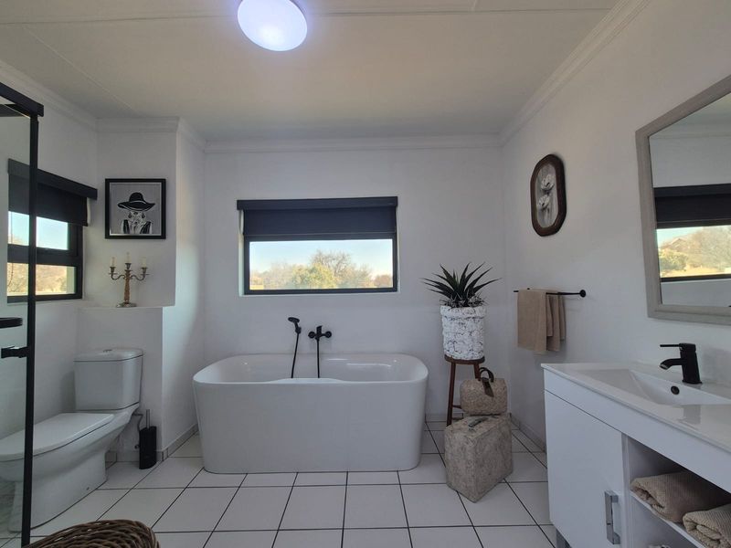 Modern bathroom featuring a sleek freestanding bathtub, black tapware, vanity cabinet with basin, and tiled flooring with neutral finishes.