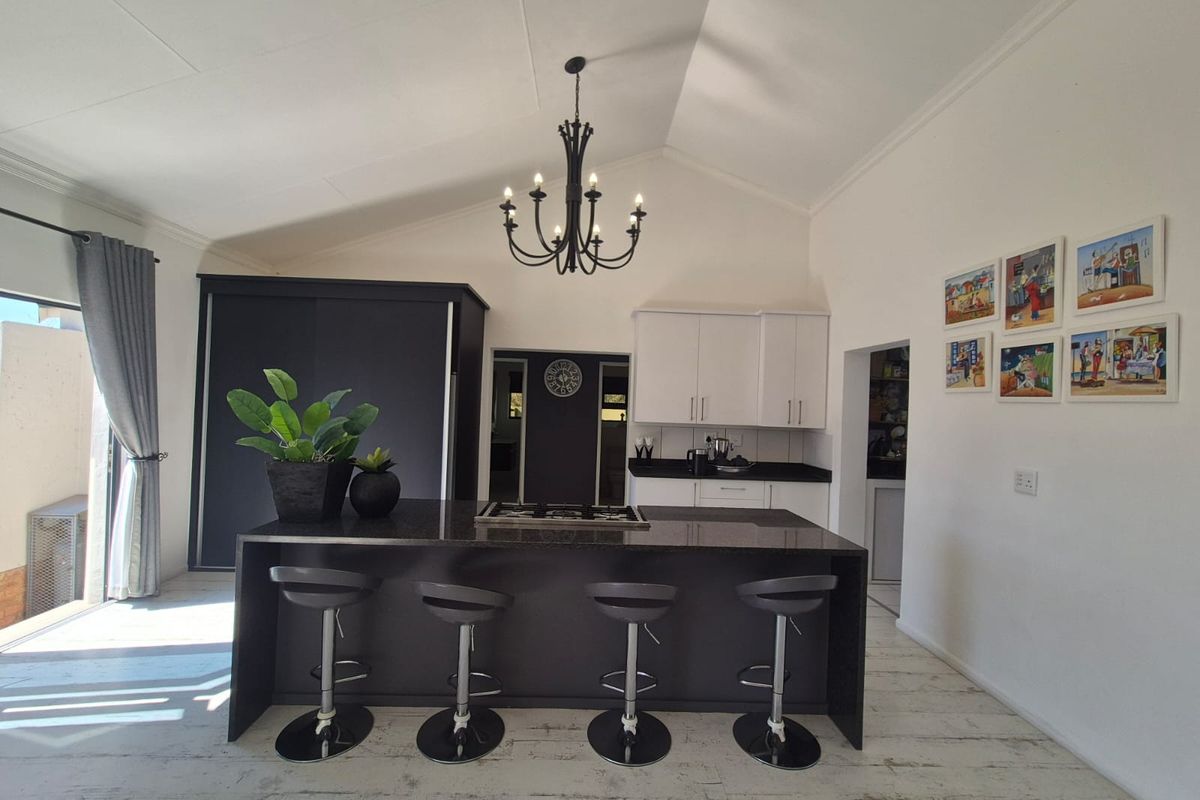 Modern kitchen featuring a large central island with a gas hob, sleek cabinetry, and a high vaulted ceiling with a feature chandelier.