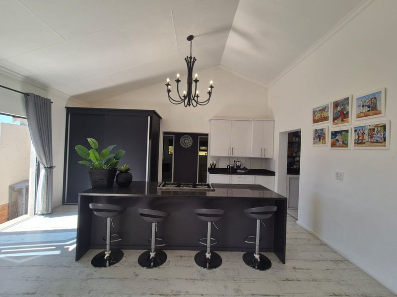 Modern kitchen featuring a large central island with a gas hob, sleek cabinetry, and a high vaulted ceiling with a feature chandelier.