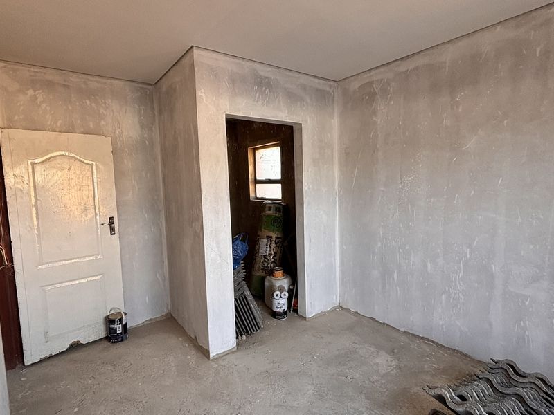 An unfinished bedroom interior featuring plastered walls, aluminium window frames, and an internal door, currently in a shell condition awaiting final flooring and paint.