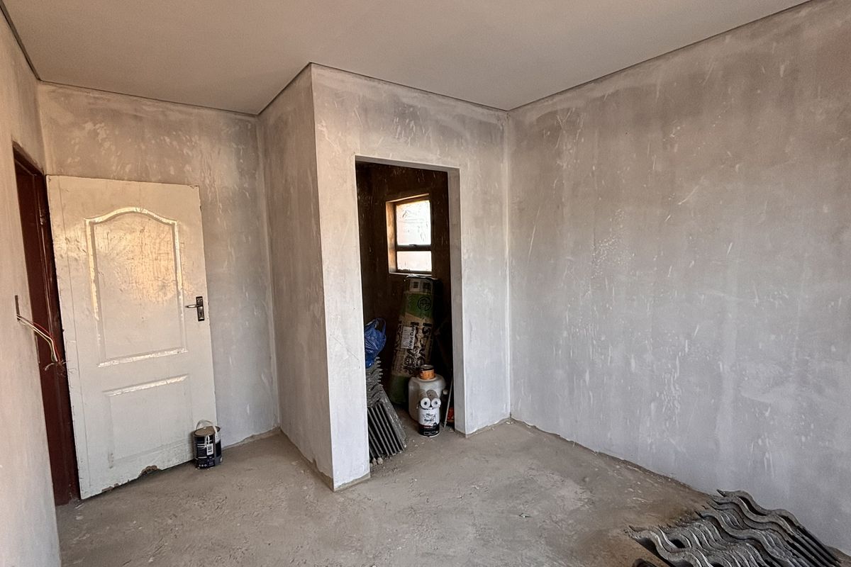 An unfinished bedroom interior featuring plastered walls, aluminium window frames, and an internal door, currently in a shell condition awaiting final flooring and paint.