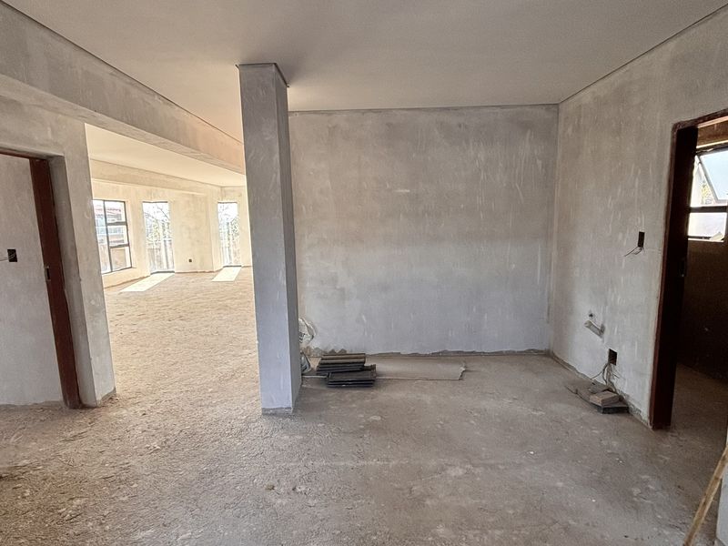 An open-plan interior space currently under construction, featuring raw plastered walls, structural columns, and unfinished flooring, offering a blank canvas for renovation.