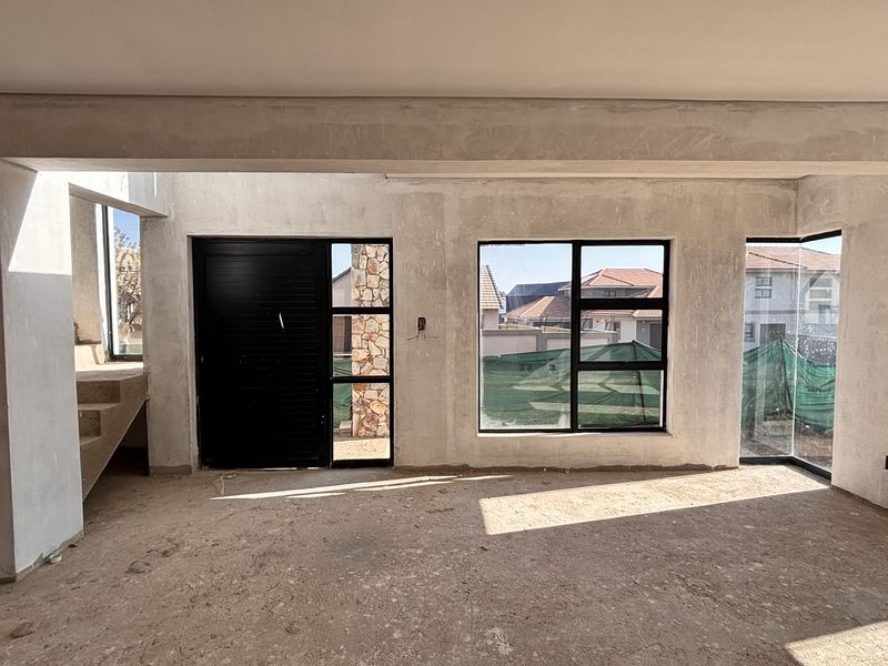 An unfinished open-plan living area featuring black aluminium window and door frames, a concrete staircase, and raw plastered walls awaiting final finishes.