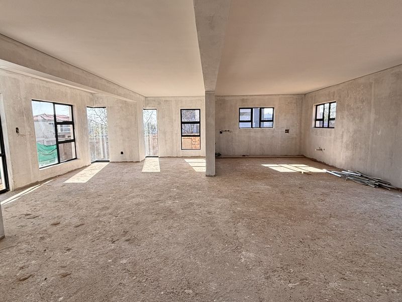 Spacious open-plan living area in a construction phase, featuring large windows, sliding doors, and structural columns, ready for final flooring and wall finishes.