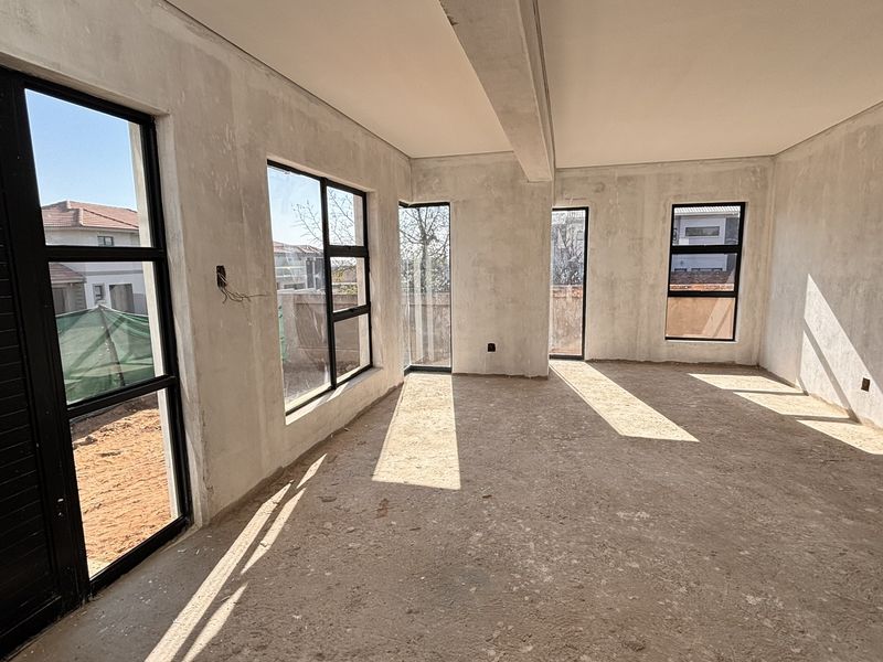 An unfinished, open-plan living area featuring black aluminium window frames and sliding doors, awaiting final flooring and wall finishes.