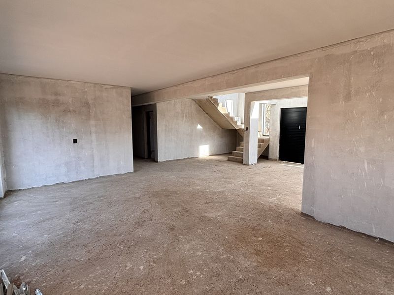 An expansive, unfinished open-plan living area featuring plastered walls, a staircase, and large sliding glass doors leading to the exterior.