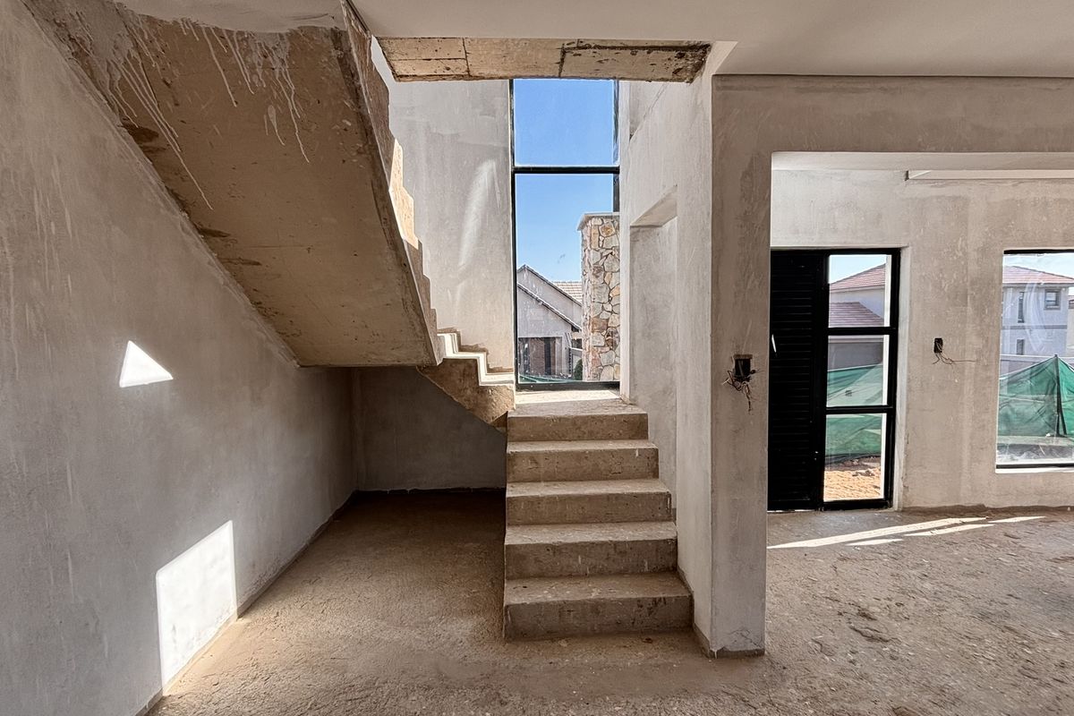 An unfinished open-plan living area featuring a concrete staircase, double-volume windows, and raw plastered walls, offering a blank canvas for custom interior finishes.