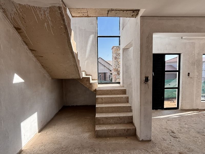 An unfinished open-plan living area featuring a concrete staircase, double-volume windows, and raw plastered walls, offering a blank canvas for custom interior finishes.