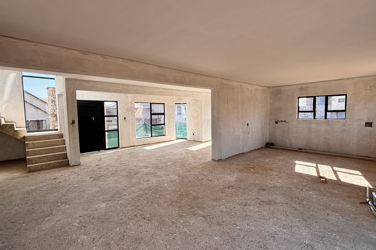 Spacious open-plan living area currently under construction, featuring plastered walls, large aluminium windows, and an internal staircase.