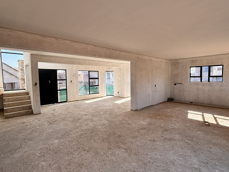 Spacious open-plan living area currently under construction, featuring plastered walls, large aluminium windows, and an internal staircase.