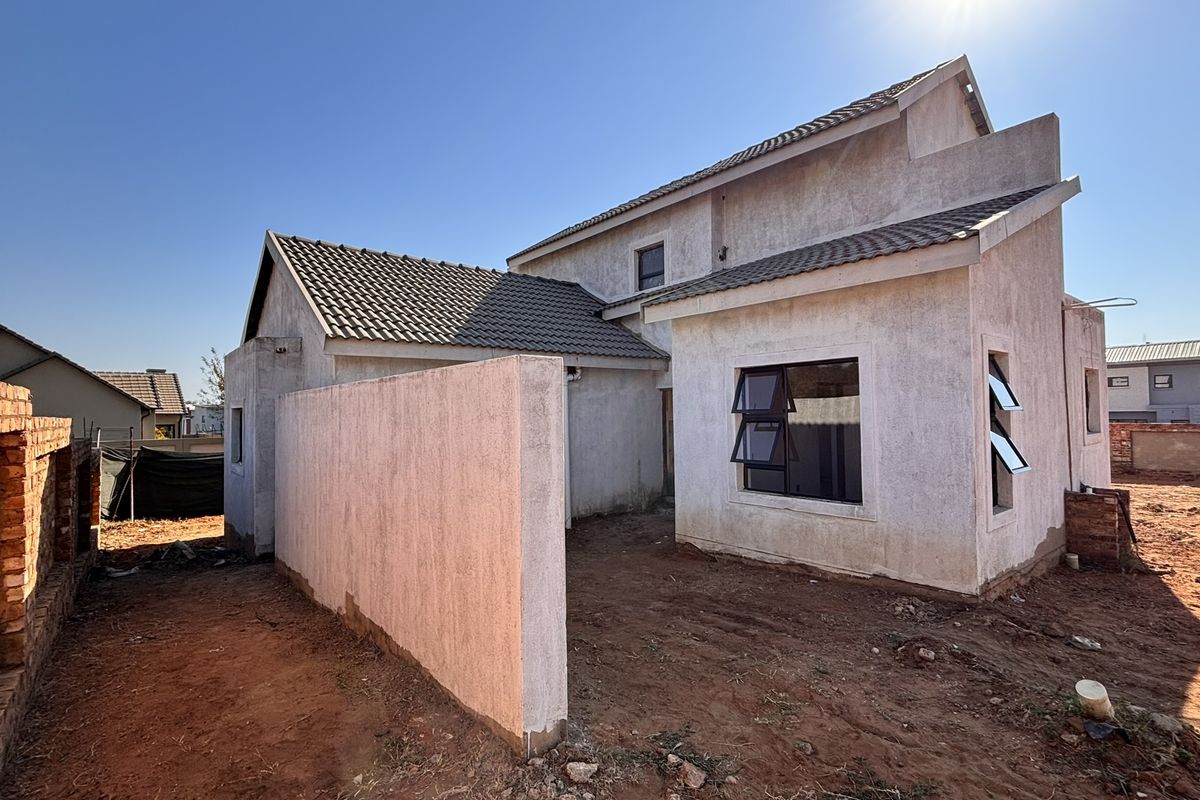 Rear view of a double-storey house under construction, featuring plastered walls, tiled roofing, and unfinished surrounding grounds.