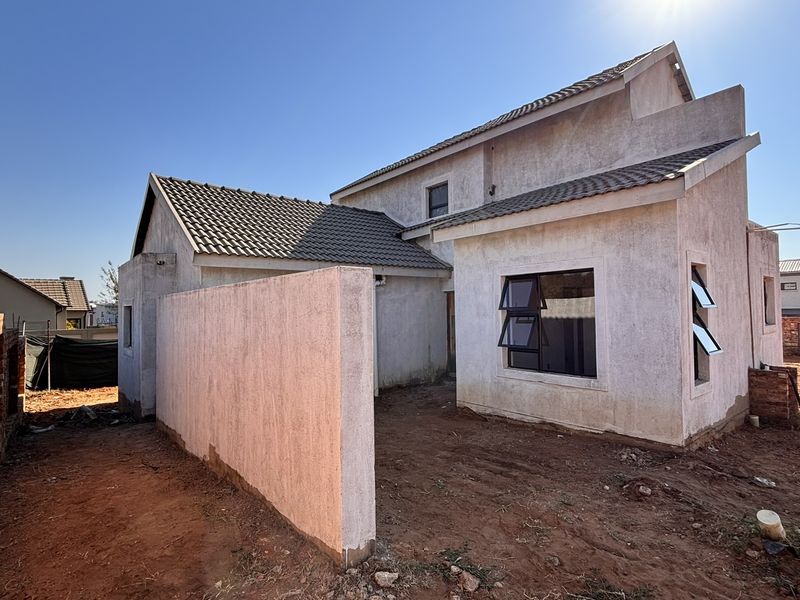 Rear view of a double-storey house under construction, featuring plastered walls, tiled roofing, and unfinished surrounding grounds.