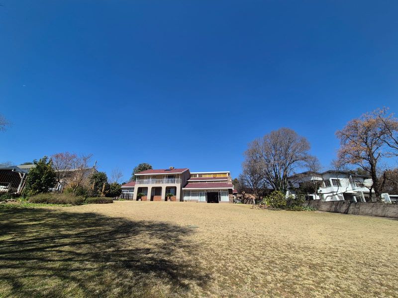 A wide-angle view of the rear elevation of a two-story house featuring a balcony, brick detailing, and a large, well-maintained lawn.