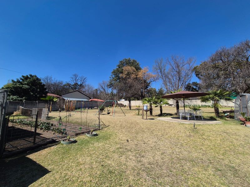 Spacious backyard garden featuring a lawn, paved patio area, vegetable garden beds, and perimeter boundary walling.