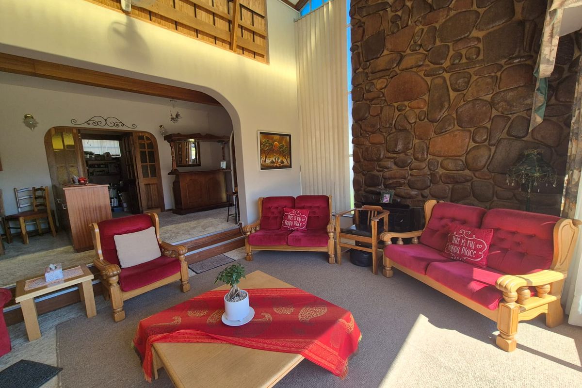 Spacious living room featuring a prominent stone fireplace, vaulted ceilings with exposed timber beams, and a raised area with a built-in bar.