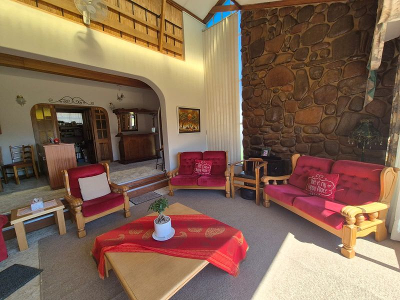 Spacious living room featuring a prominent stone fireplace, vaulted ceilings with exposed timber beams, and a raised area with a built-in bar.