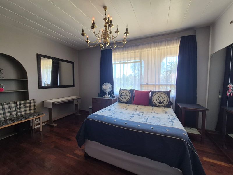 A spacious bedroom featuring polished hardwood flooring, a classic chandelier, and a built-in arched shelving unit, offering a comfortable and functional living space.