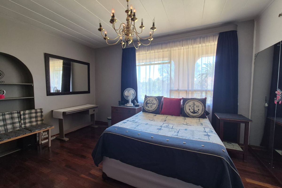 A spacious bedroom featuring polished hardwood flooring, a classic chandelier, and a built-in arched shelving unit, offering a comfortable and functional living space.